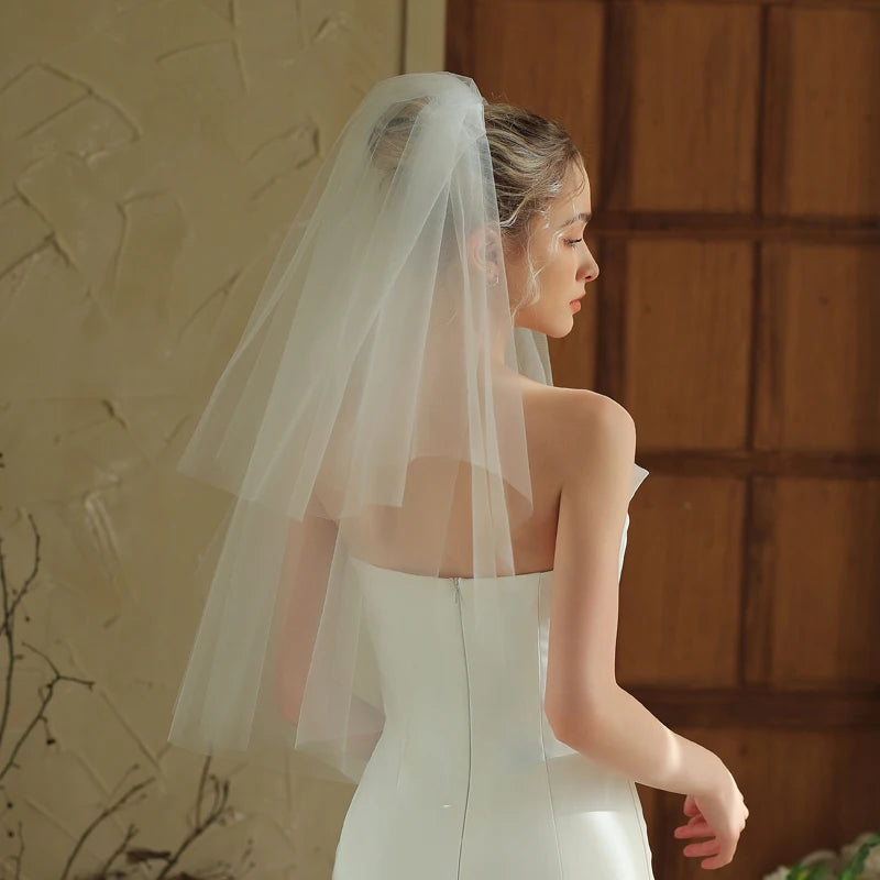 Woman wearing a white wedding dress with a veil against a warm-toned wall.