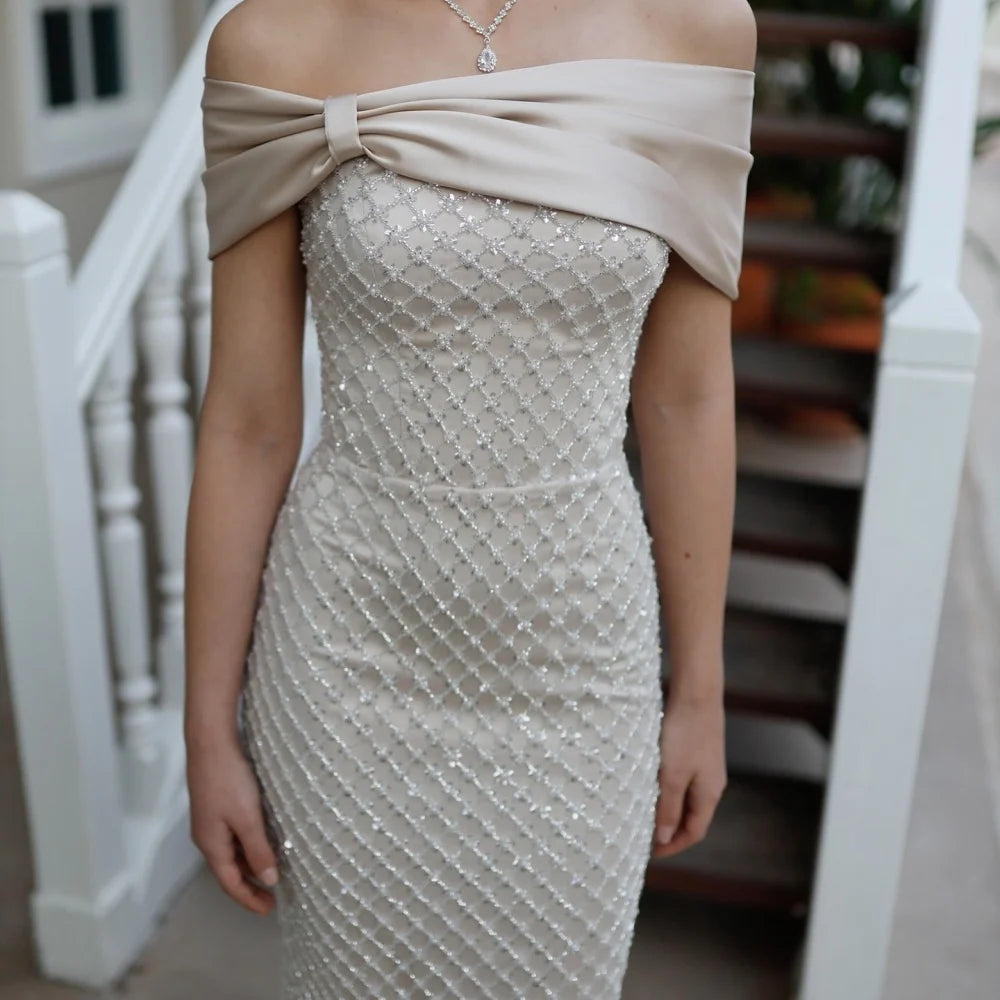 Beige off-shoulder dress with a large bow detail on a blurred staircase background