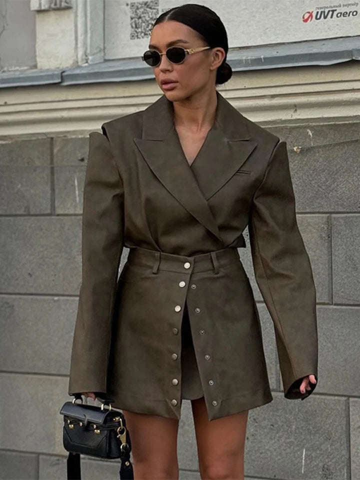 Woman wearing a brown coat and skirt set against a gray building background