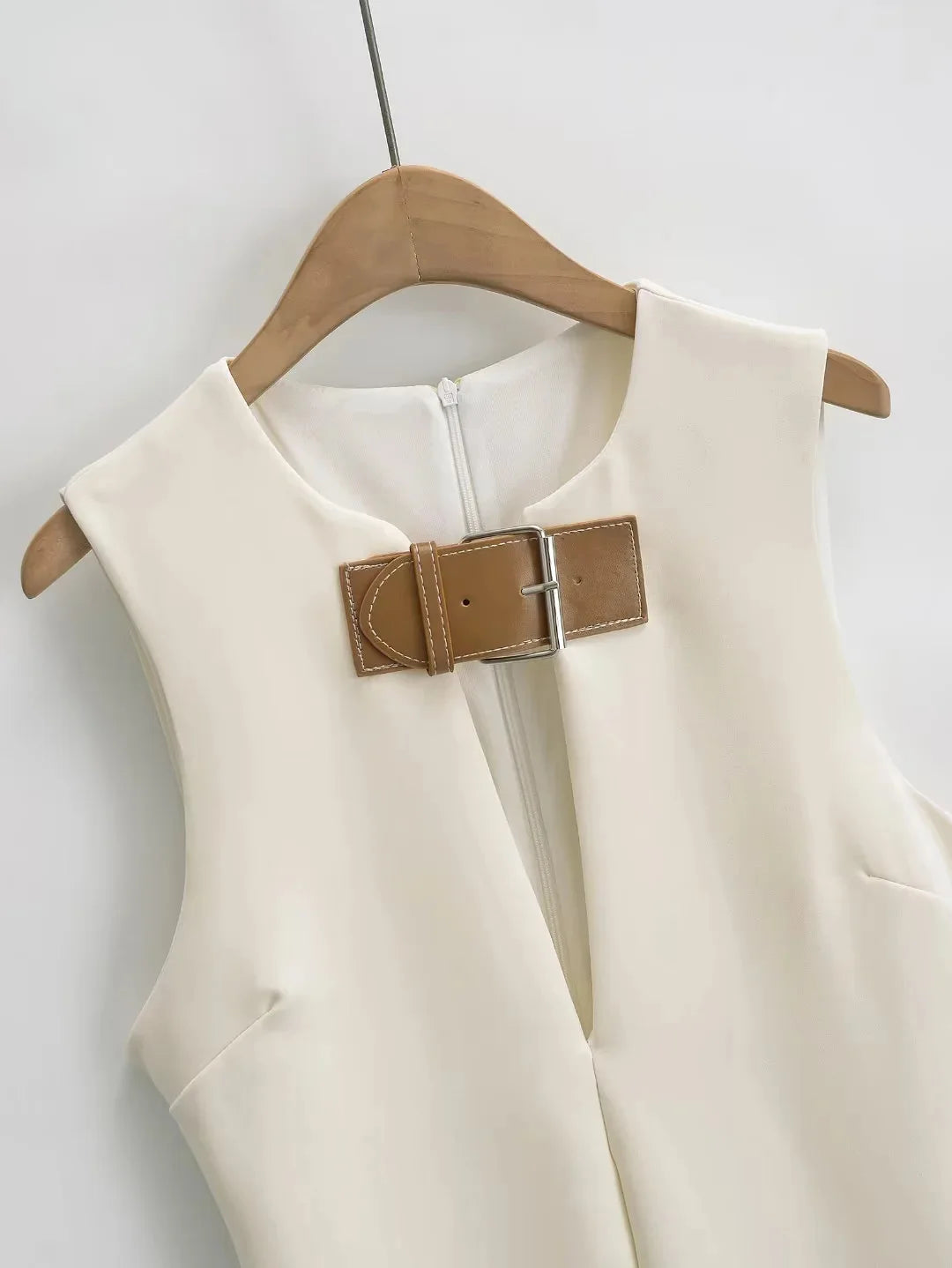 White sleeveless top with a brown belt on a wooden hanger against a white background