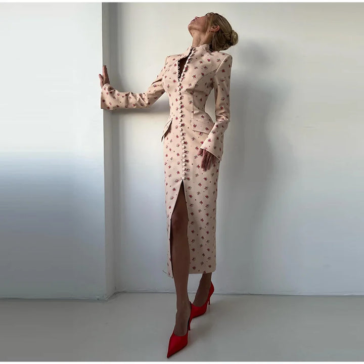 Woman in a patterned dress with a high slit standing against a plain wall.