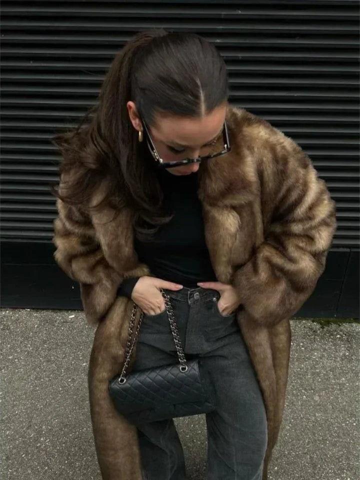Person wearing a fur coat and holding a black handbag against a dark background