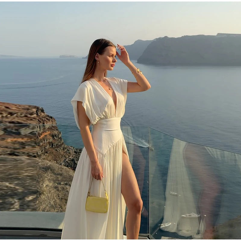 Woman in a white dress with a yellow handbag standing on a cliff overlooking the ocean.