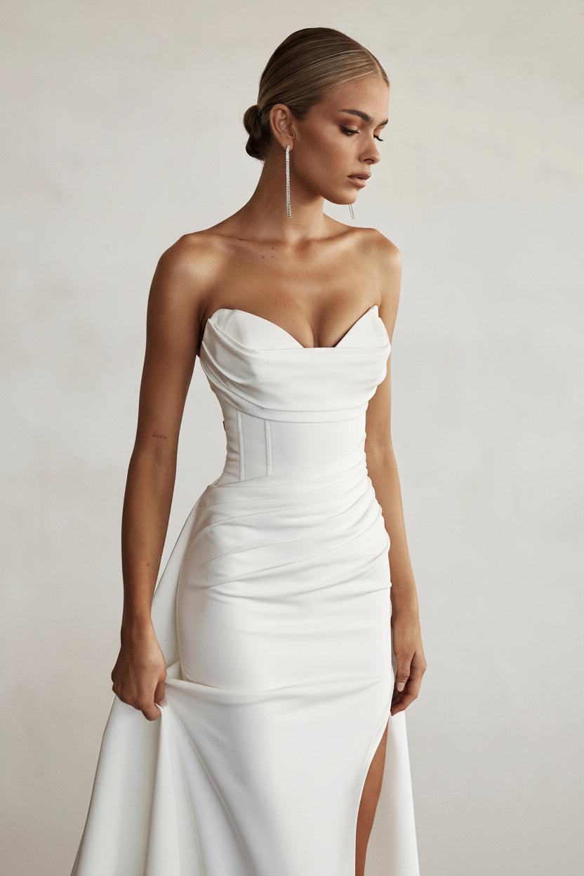Woman wearing a white strapless dress against a plain background