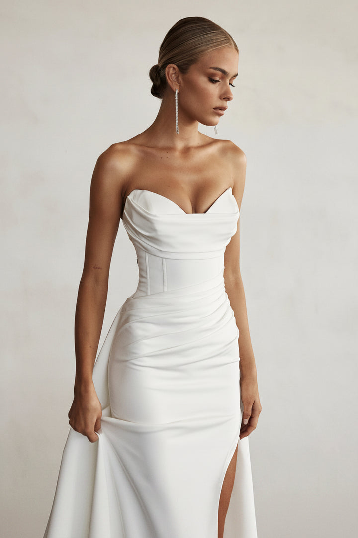 Woman wearing a white strapless dress against a plain background