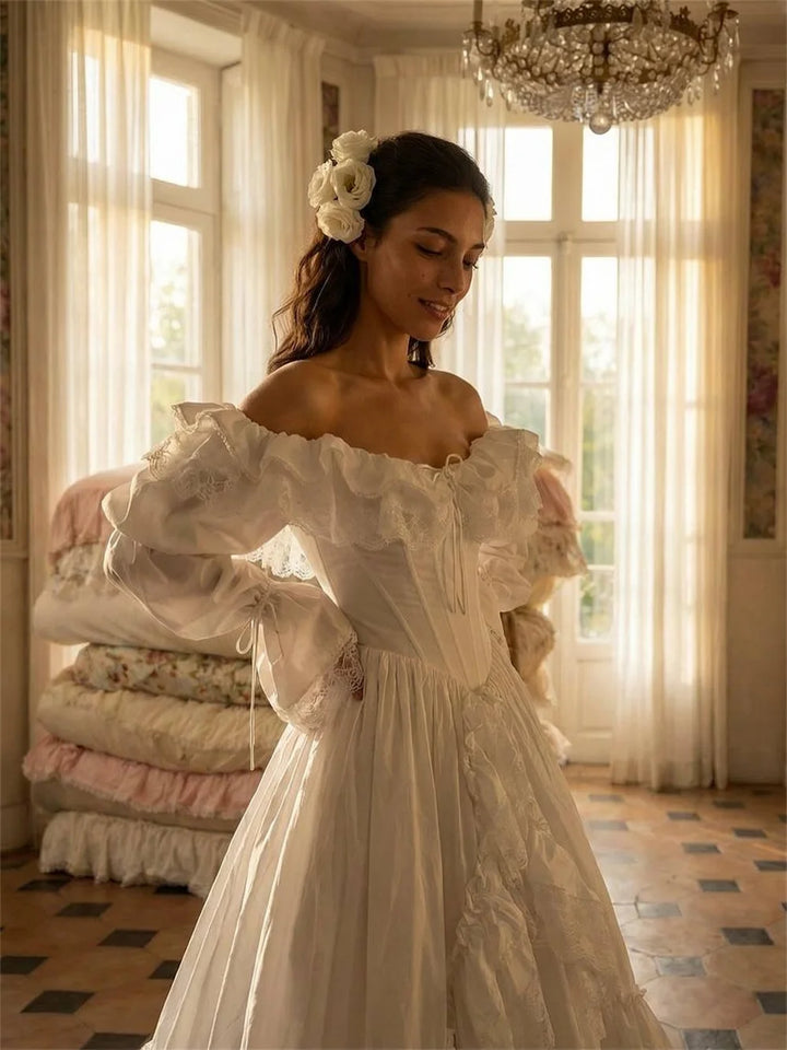Woman in a white lace dress standing in a room with large windows and a chandelier.