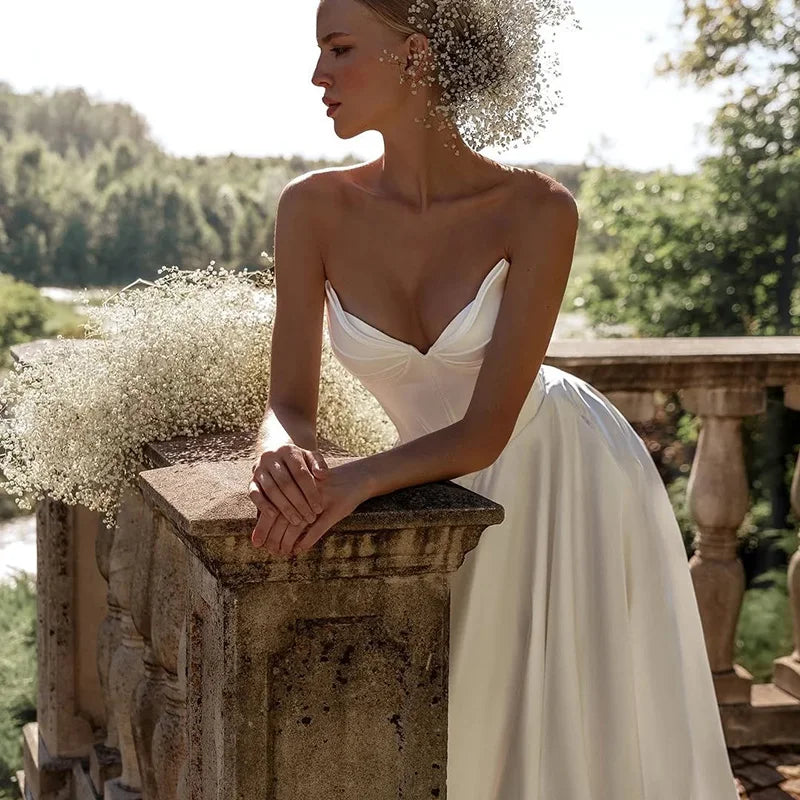 Woman in a white wedding dress sitting on a stone railing with greenery in the background