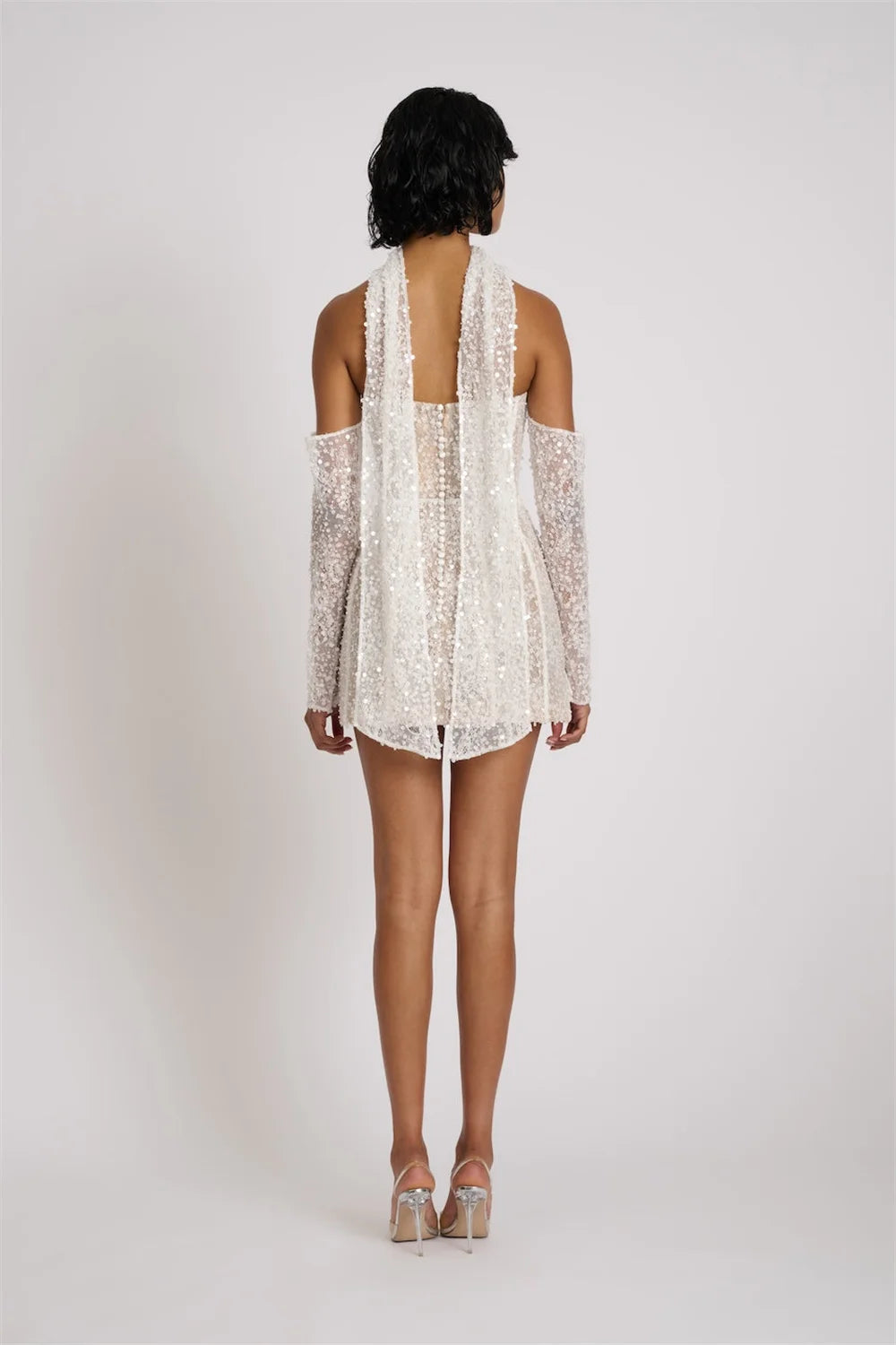 Woman wearing a white lace dress with thin straps on a plain background