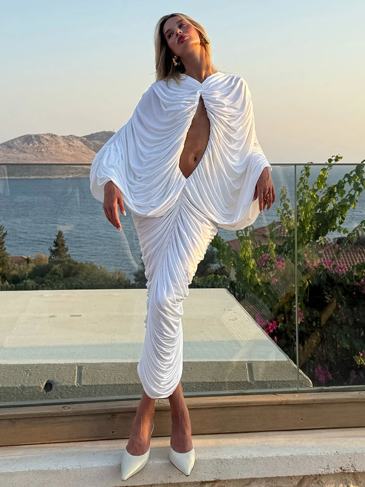 Woman in a white dress standing on a balcony with a scenic view of water and mountains.