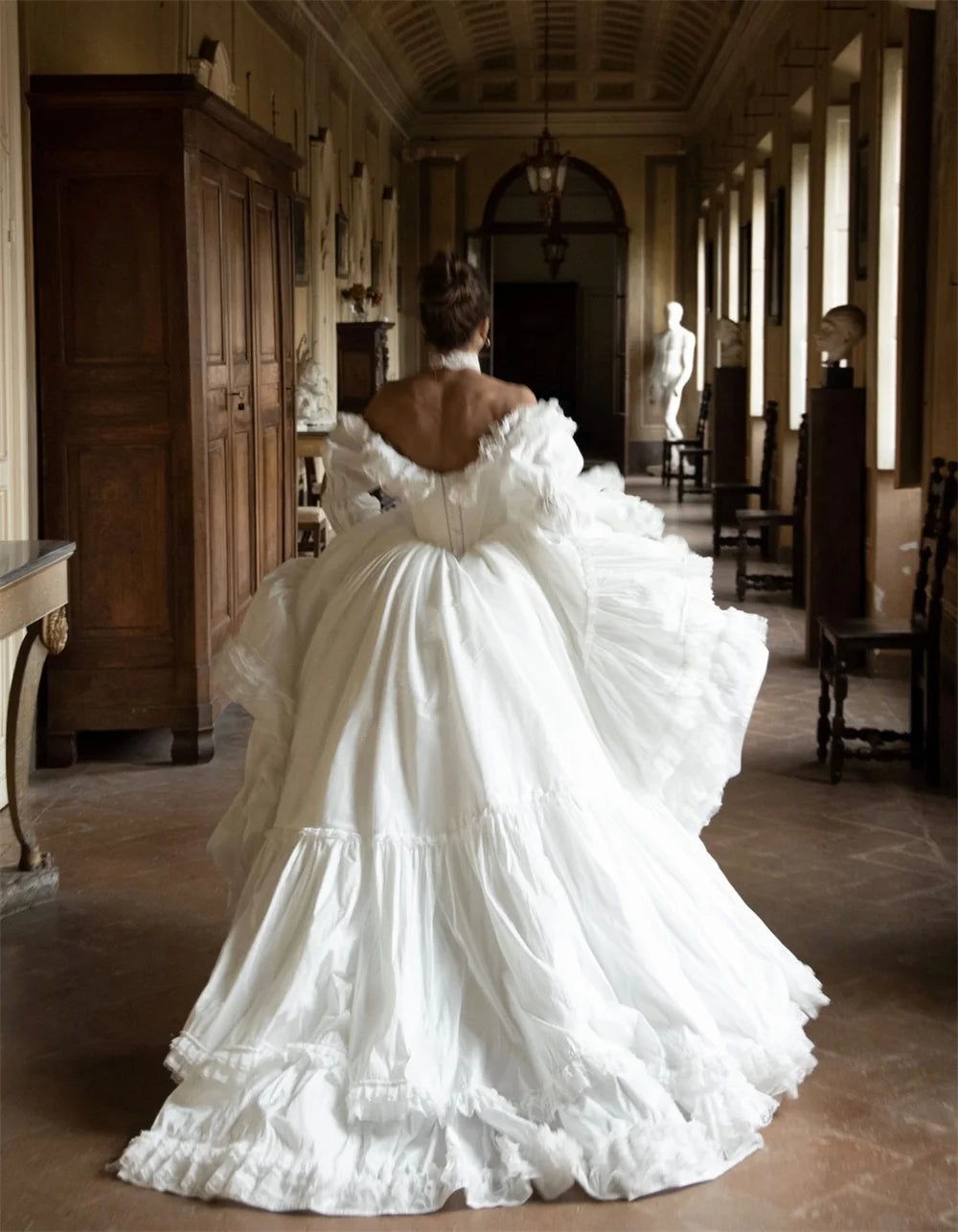 Person wearing a white, elaborate gown in a grand hallway.