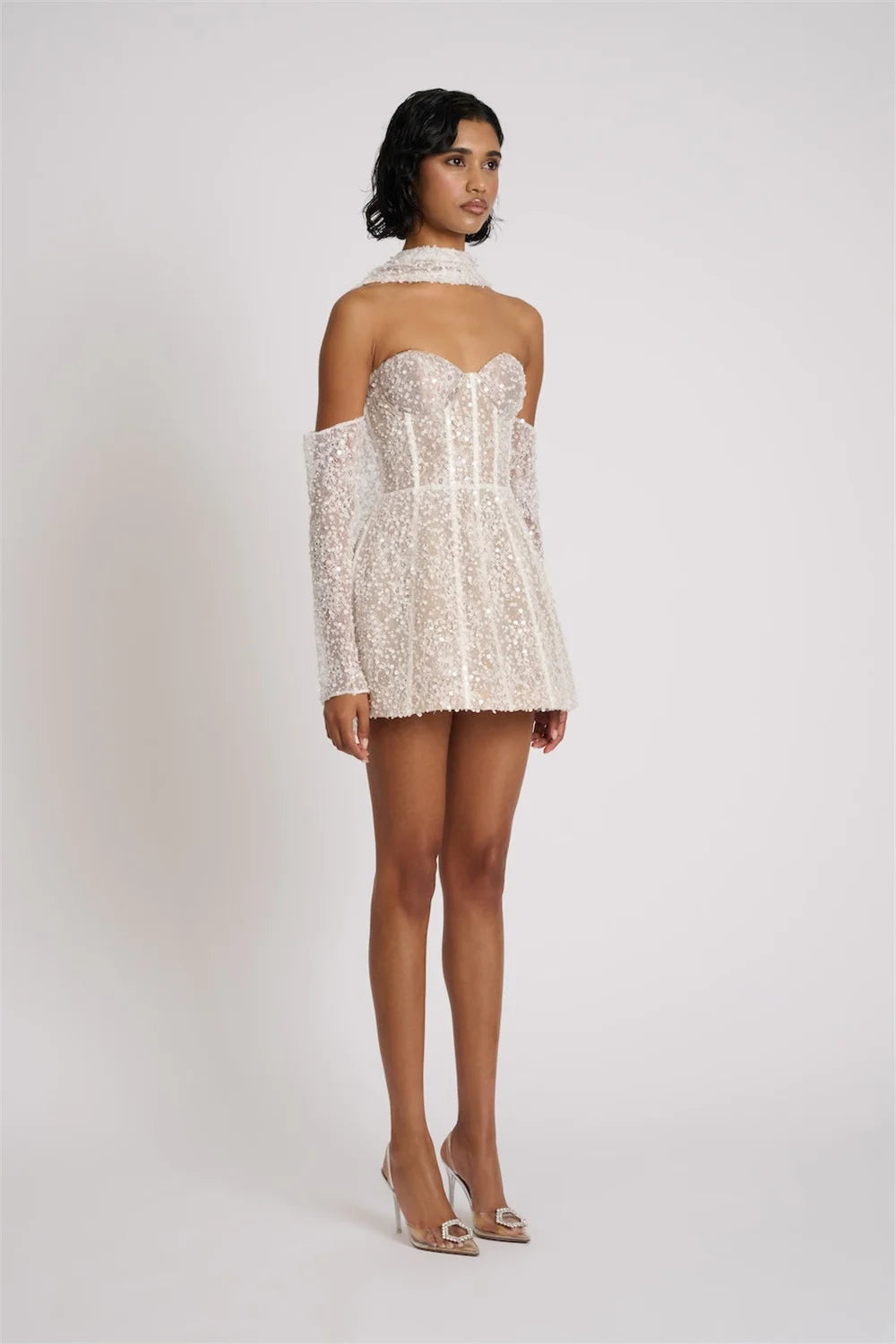 Woman wearing a white lace dress with thin straps on a plain background