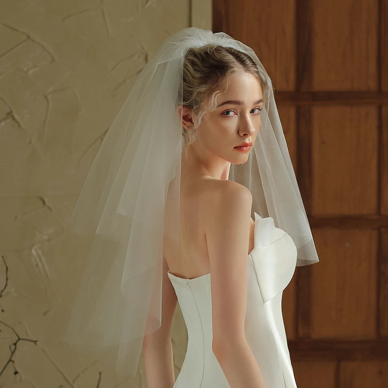 Woman in a white wedding dress with a veil against a warm-toned wall.
