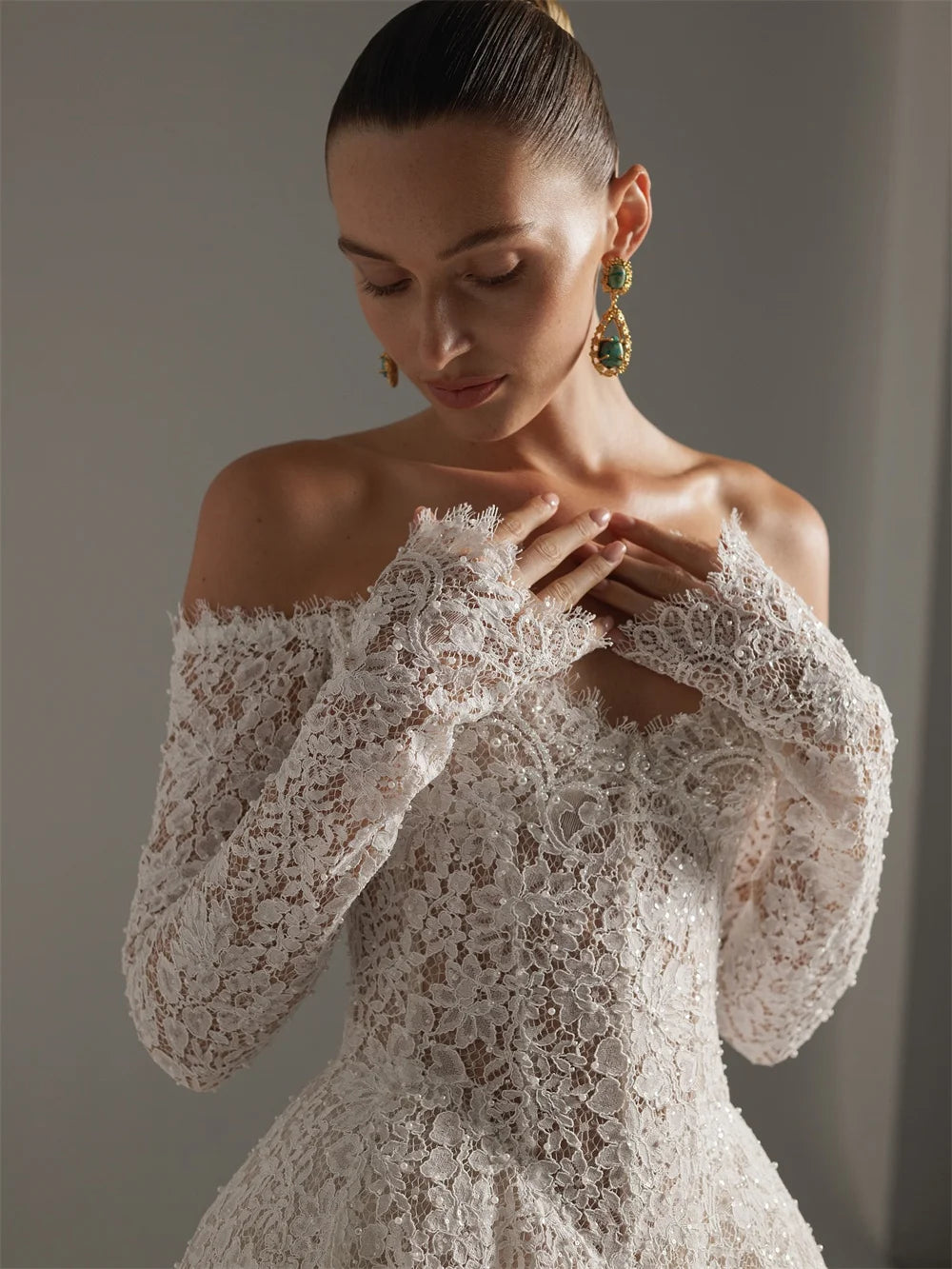 Woman wearing a lace off-shoulder dress with long sleeves against a neutral background