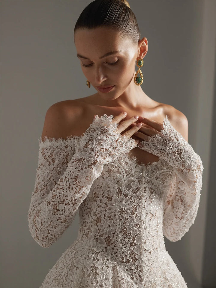 Woman wearing a lace off-shoulder dress with long sleeves against a neutral background