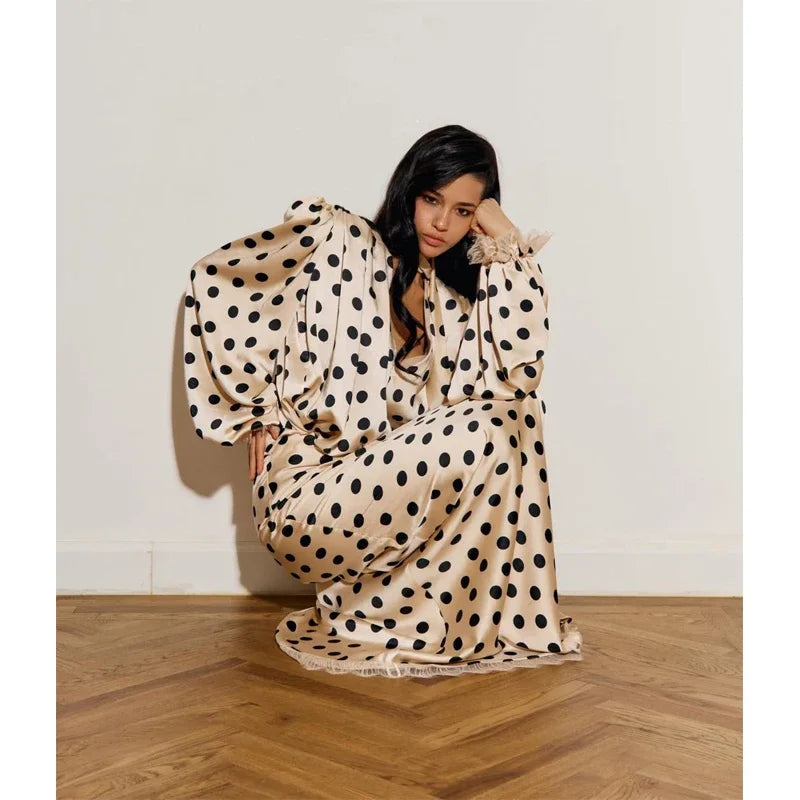 Woman wearing a polka dot dress sitting on a wooden floor against a white wall.