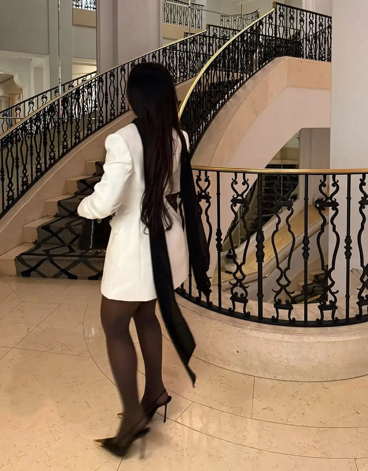 Woman in a white coat standing in front of an elegant staircase