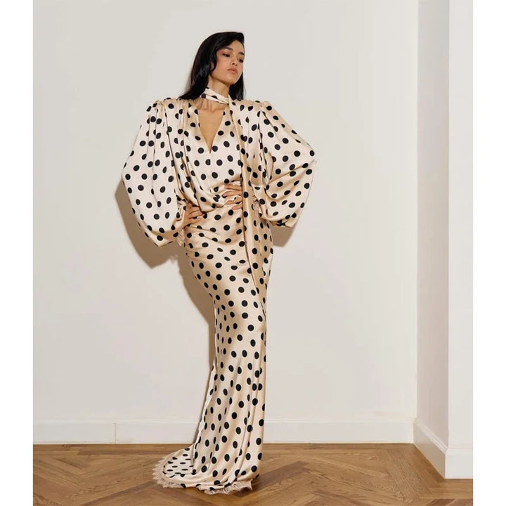 Woman wearing a polka dot dress standing against a white wall.