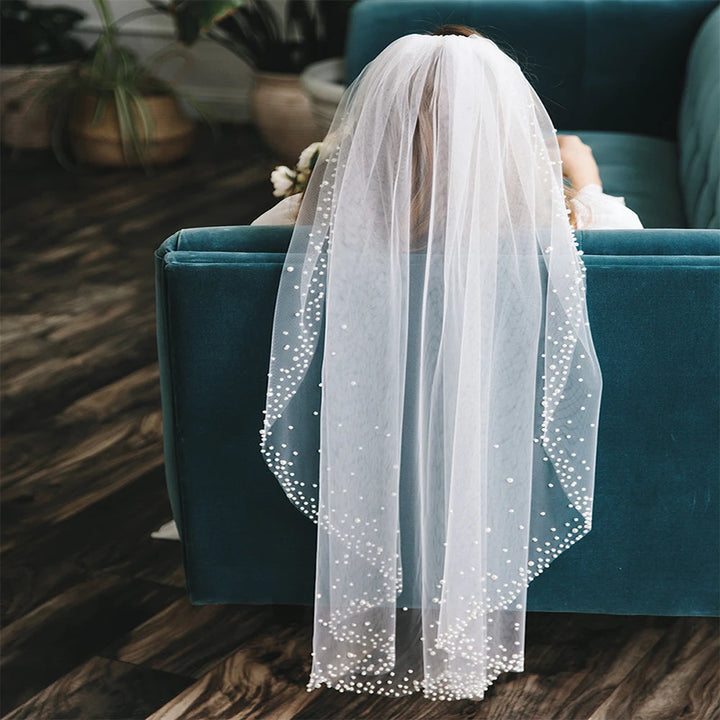 White veil with sparkling dots draped over a person sitting on a teal couch.