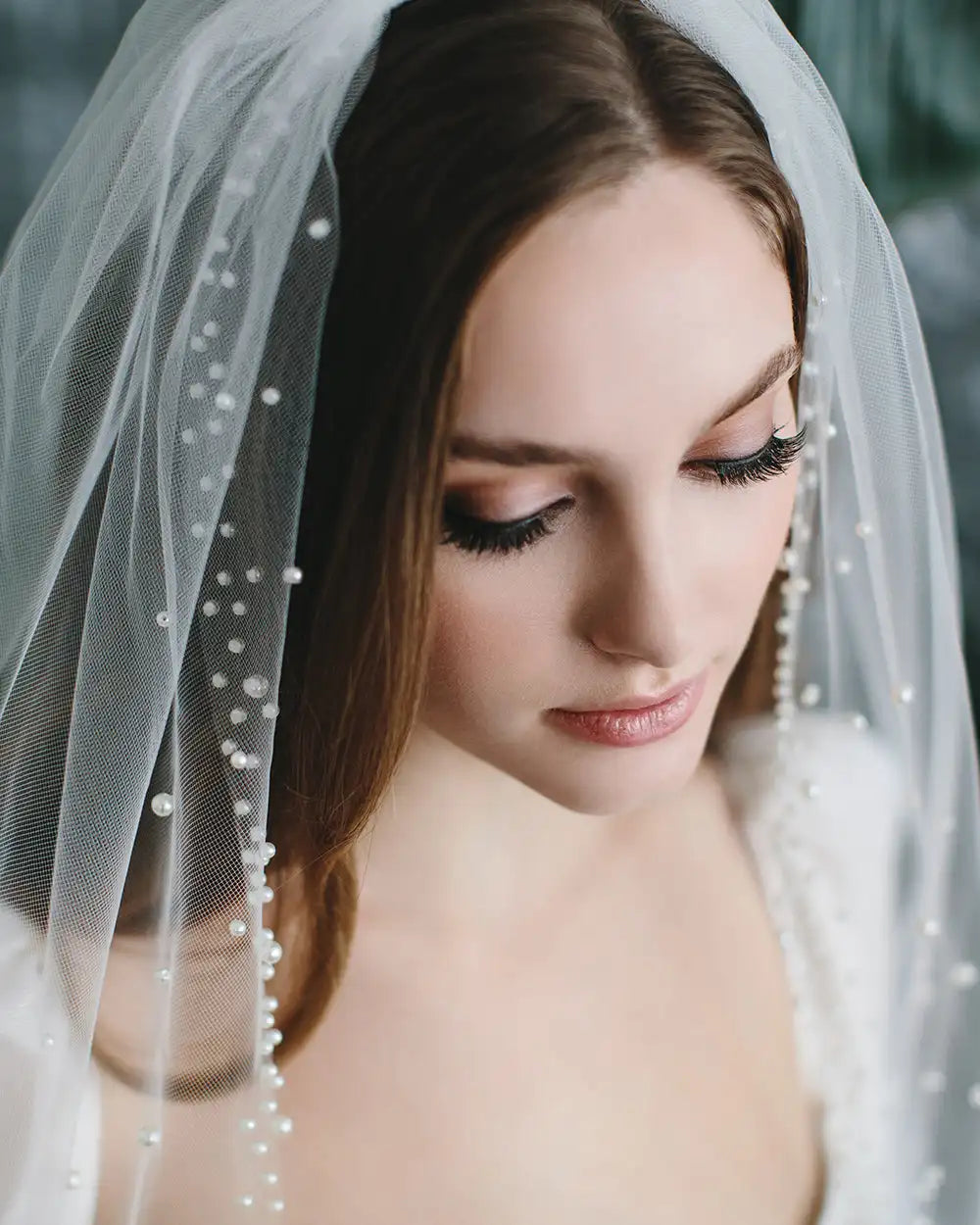 Woman wearing a white veil with pearl accents, looking down.