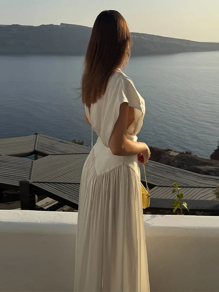 Woman in a white dress standing on a rooftop overlooking a scenic view of water and mountains.