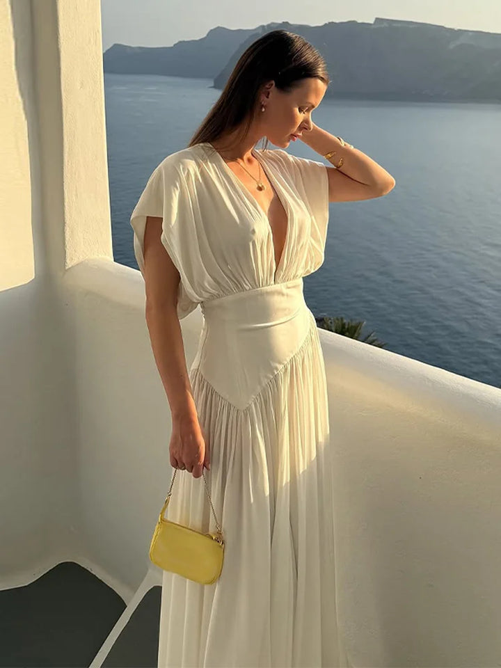 Woman in a white dress with a yellow handbag standing on a balcony overlooking a scenic view.