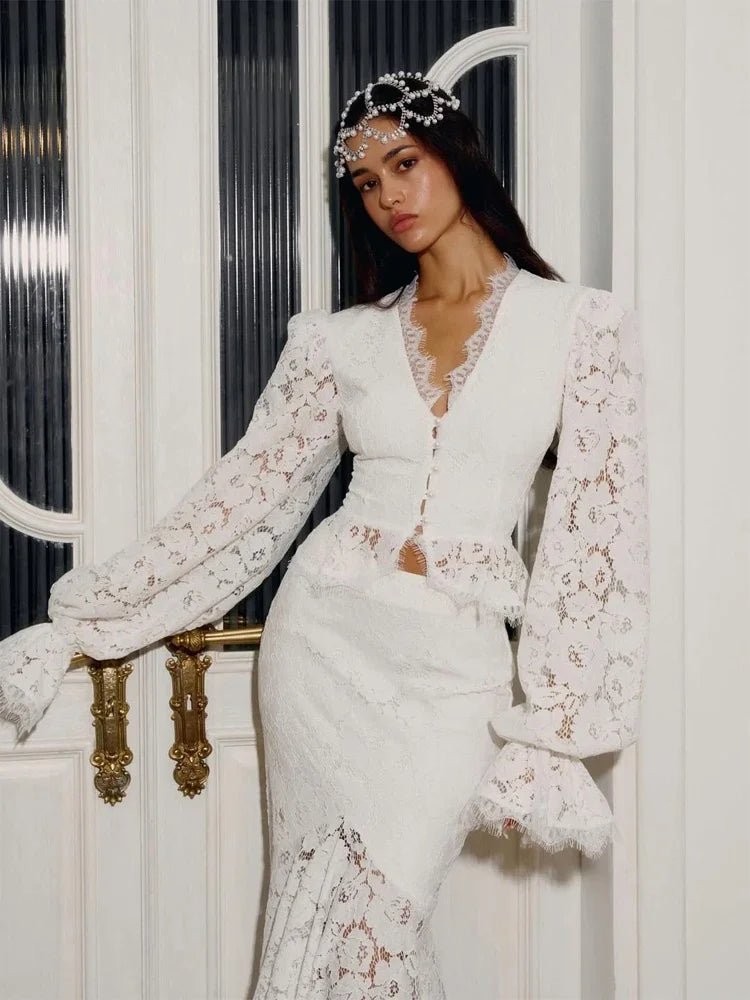 Woman in a white lace outfit standing against a decorative door.