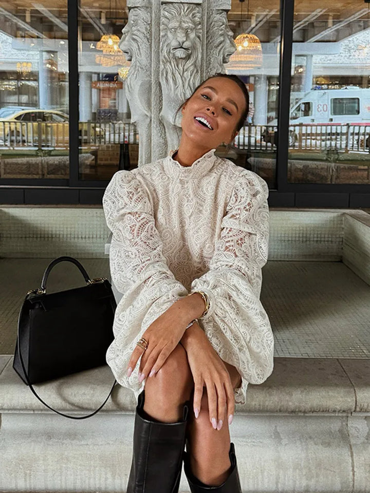 Woman in a white lace dress and black knee-high boots sitting on steps with a black handbag.