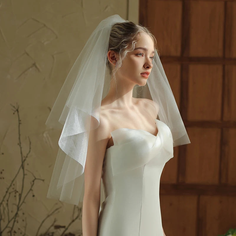 Woman wearing a white wedding dress with a veil against a warm-toned wall.