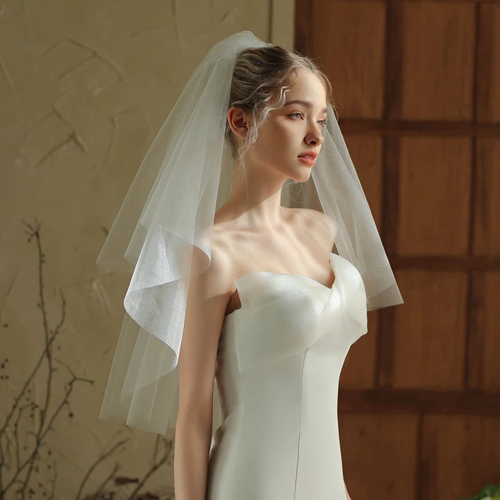 Woman wearing a white wedding dress with a veil against a warm-toned wall.