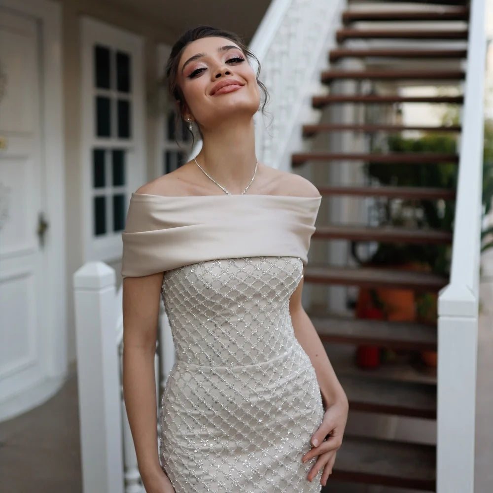 Woman in a beige off-shoulder dress standing outdoors near a staircase.