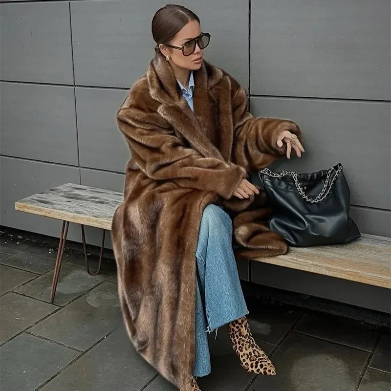 Woman in a brown fur coat sitting on a bench with a black handbag.