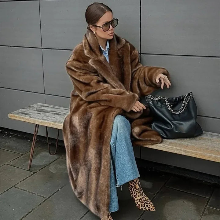 Woman in a brown fur coat sitting on a bench with a black handbag.
