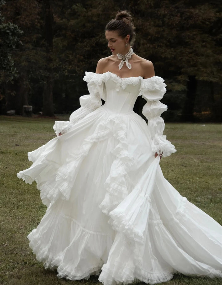 Woman in a white off-shoulder gown with puffed sleeves standing outdoors.