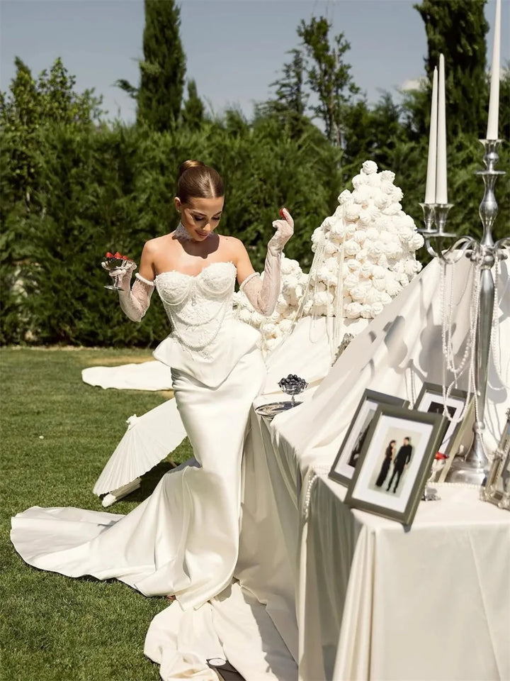 Woman in a white wedding dress standing next to a decorated table outdoors.