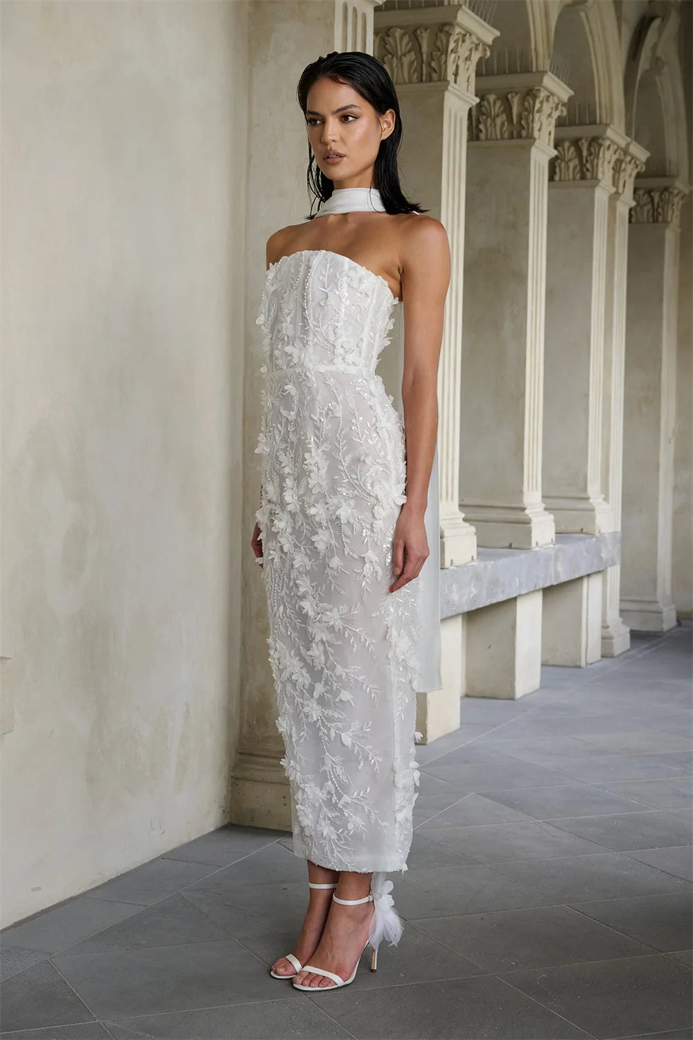 Woman in a strapless white lace wedding dress standing in an elegant hallway.
