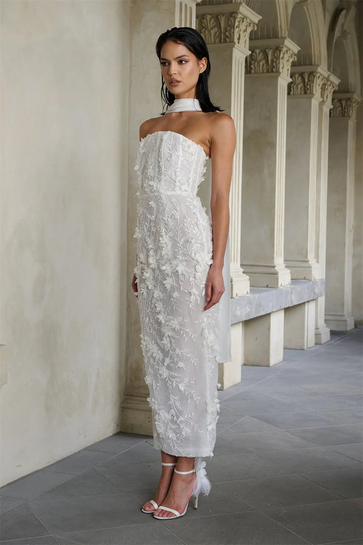 Woman in a strapless white lace wedding dress standing in an elegant hallway.
