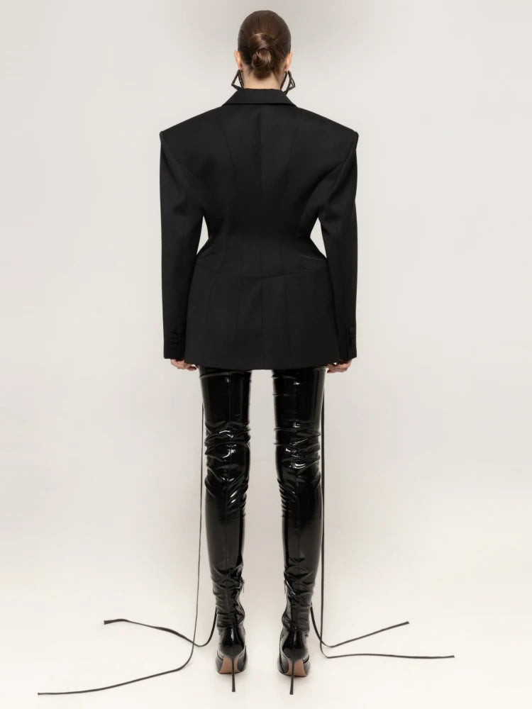 Person wearing a black blazer and shiny black pants on a white background