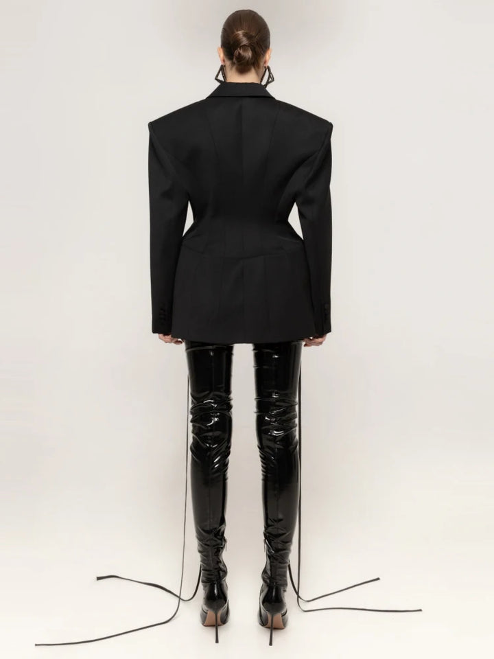 Person wearing a black blazer and shiny black pants on a white background