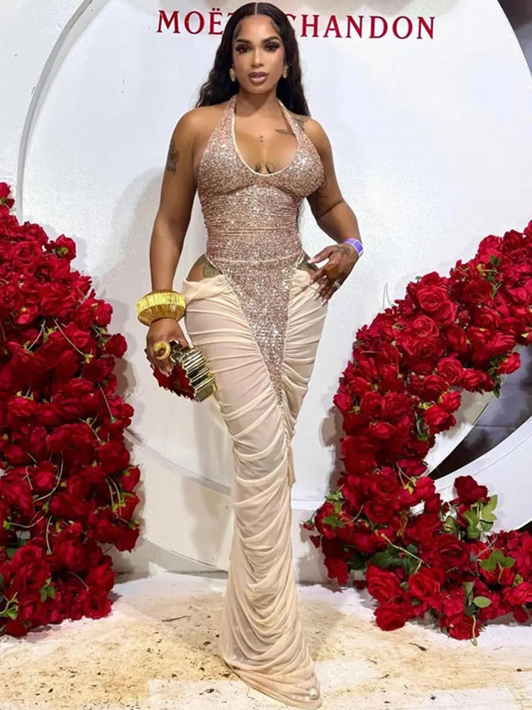 A woman stands in a glamorous setting wearing a floor-length champagne beige gown with a heavily embellished sequined bodice and draped skirt. Red rose arrangements flank her, and a white backdrop features the Moët &amp; Chandon logo at the top.