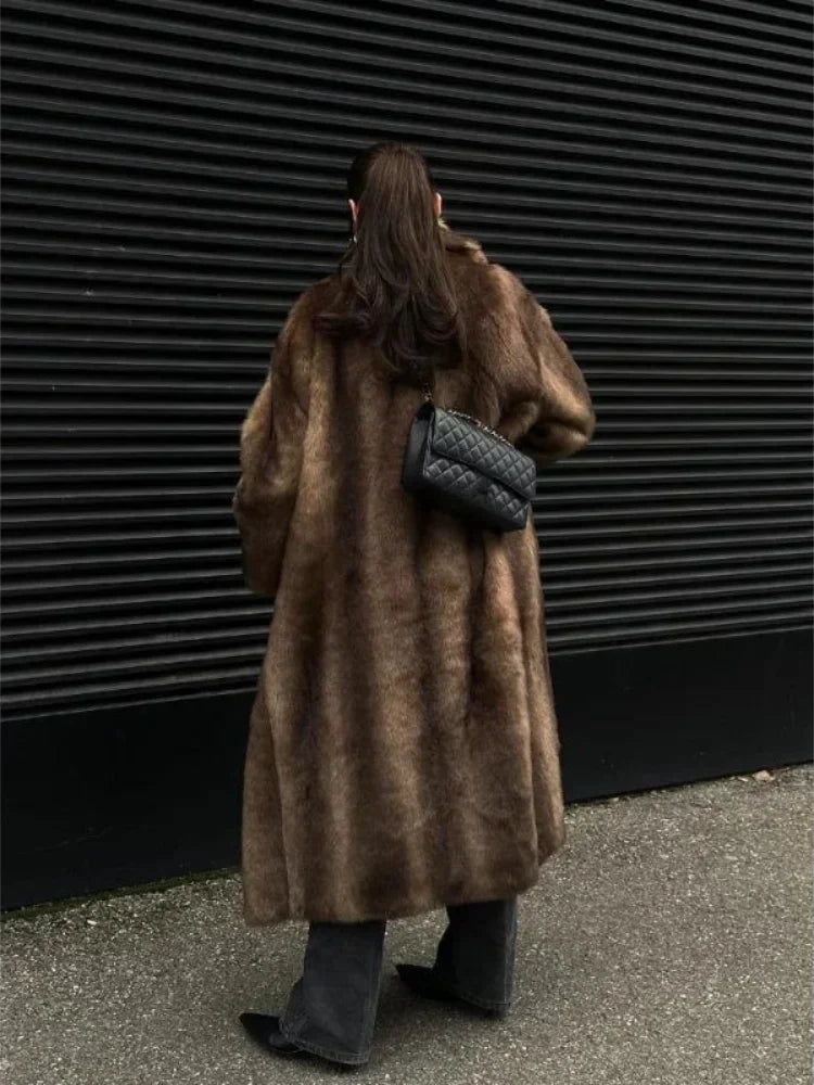Person wearing a long brown fur coat against a dark textured wall.