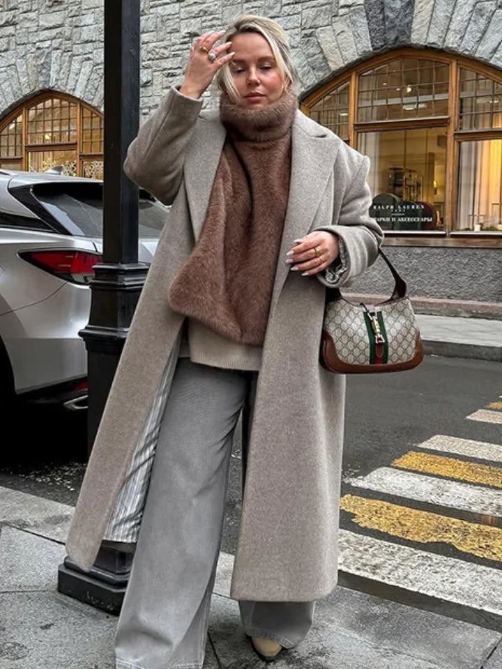 Person wearing a long coat, scarf, and holding a Gucci handbag on a city street.