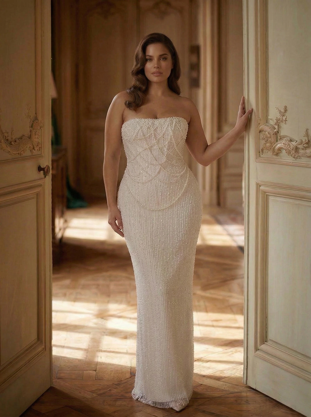 Woman in a strapless, beaded evening gown standing in an elegant room with wooden floors and ornate doors.